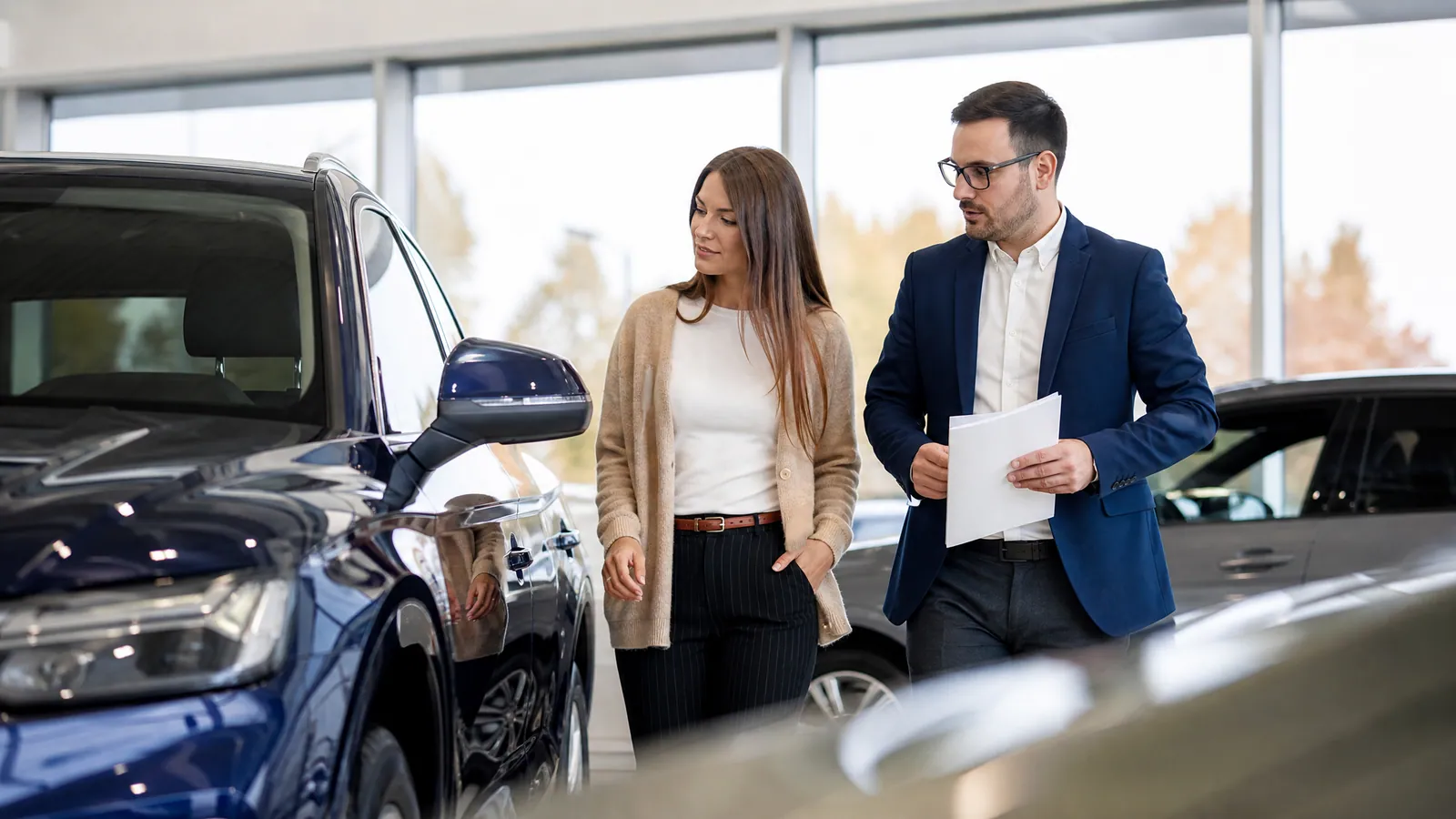 Sprzedawca i klient oglądają nowy samochód w jasnym salonie dealerskim